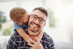 Father with glasses being kissed on the cheek by son.