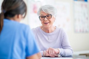 Senior woman with glasses talking to nurse.