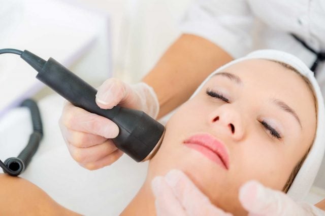 Woman getting ultrasonic and laser face treatment at beauty salon.